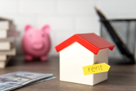 A small toy house with a yellow sticky note labeled "rent" attached to it. Renting property concept.